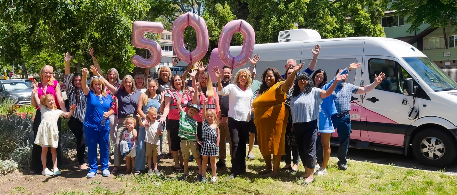 Pro-Life Utah staff, volunteers and children cheering with pink balloons spelling 500 in front of a pink-and-white Pro-Life Utah van