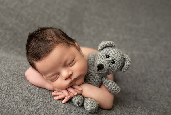 A newborn baby sleeping peacefully with a small gray knitted teddy bear