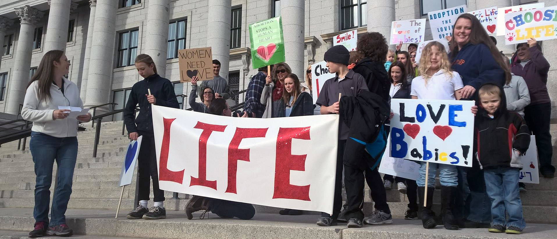 Marchers gathered on the steps of the Utah State Capitol with a large red LIFE banner and homemade signs